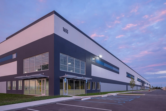 Front corner entrance of a speculative industrial building at dusk with blue and purple clouds in the sky